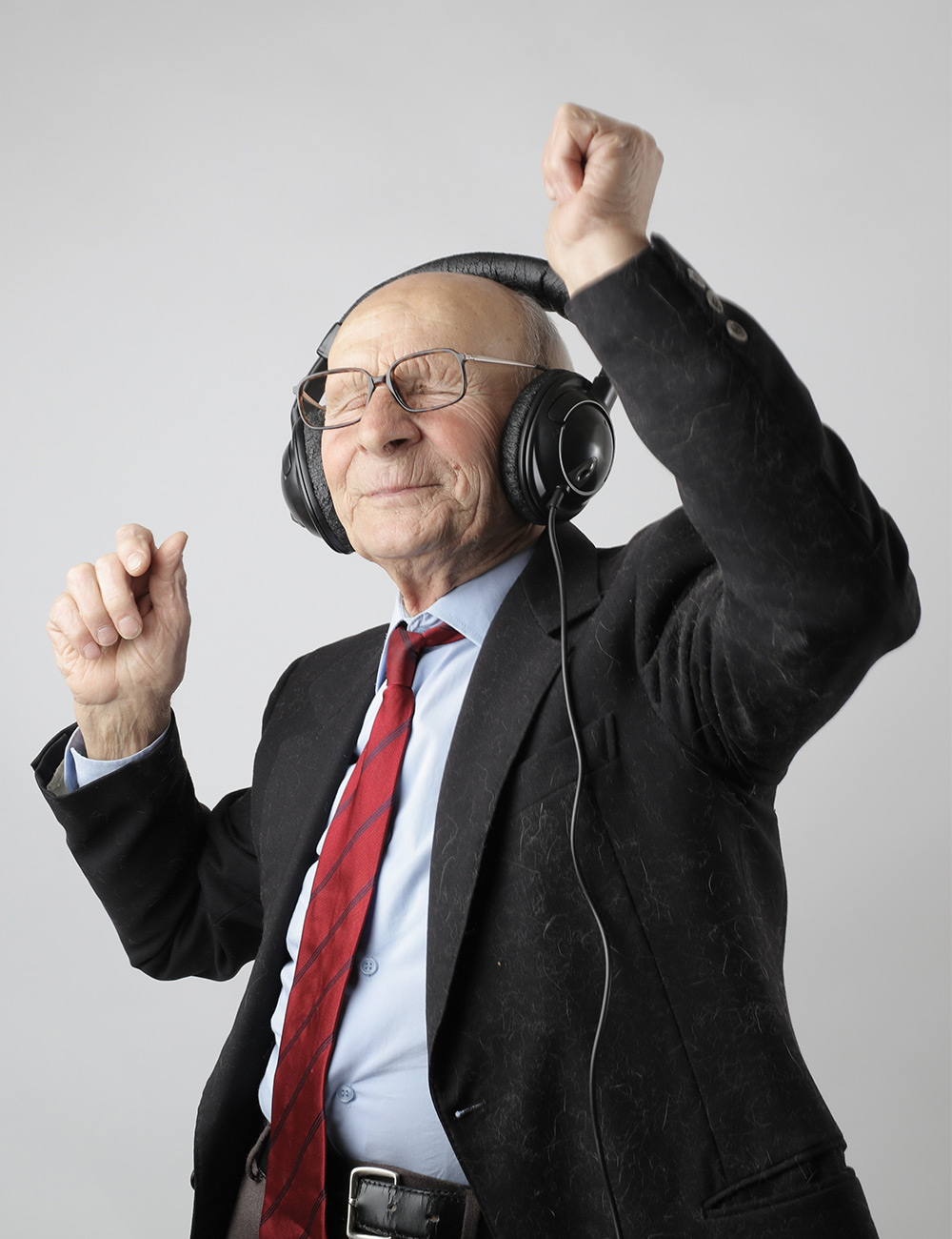 An older man in a suit and tie is listening to music.