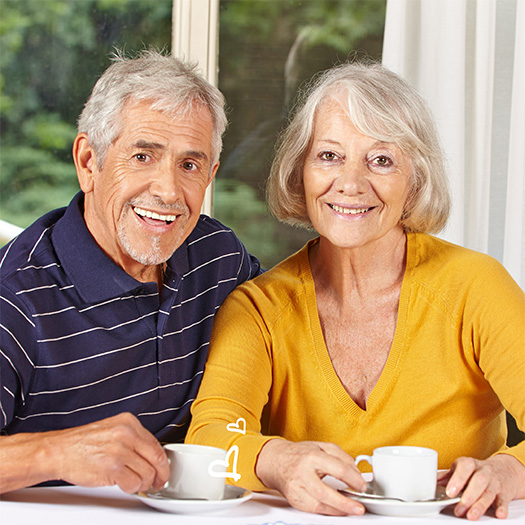 An older couple sitting at a table with cups of coffee.