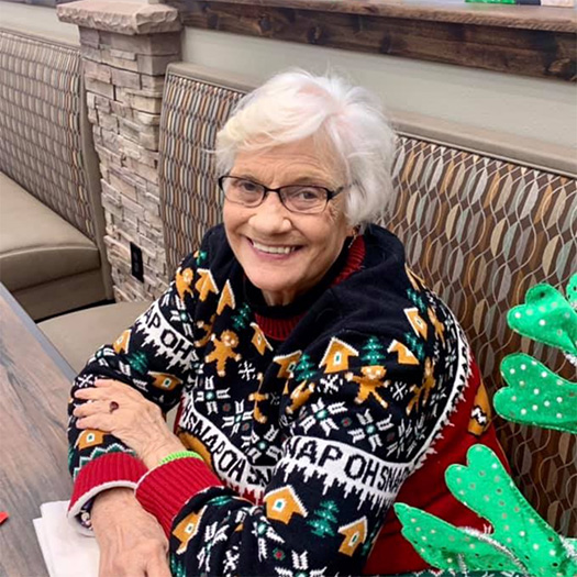 An older woman in an Christmas sweater sitting at a table.